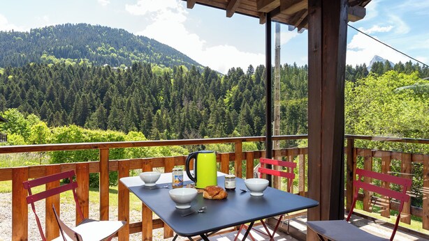 Un balcon avec une table préparée pour le petit-déjeuner, donnant sur une montagne boisée.