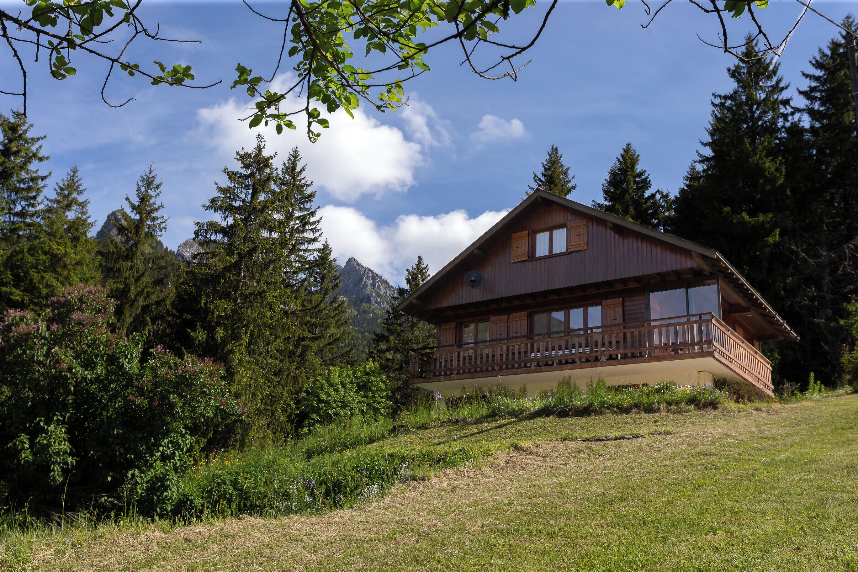 A wooden cabin with a balcony, surrounded by trees and mountains.