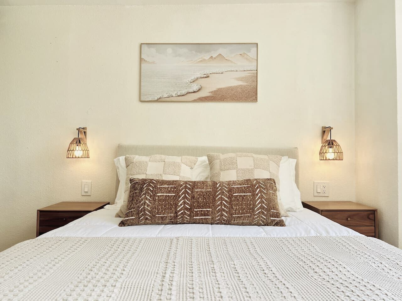 Un letto rifatto con cura, cuscini decorati, un quadro appeso al muro e due lampade ai comodini.