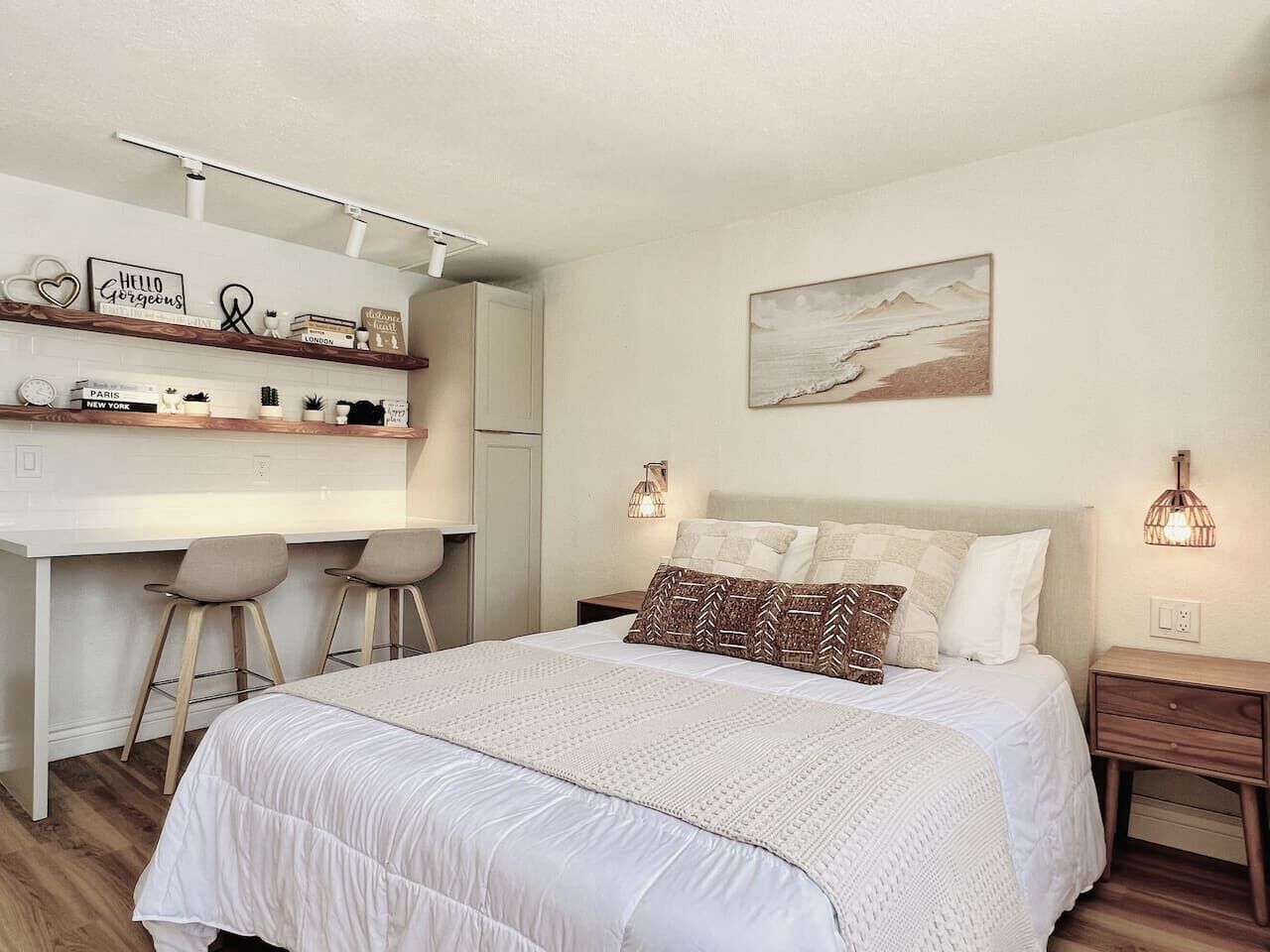 Ein modernes Schlafzimmer mit einem großen Bett, einer Schreibtischzeile mit zwei Stühlen und einem an der Wand befestigten Regal mit Dekorationen.