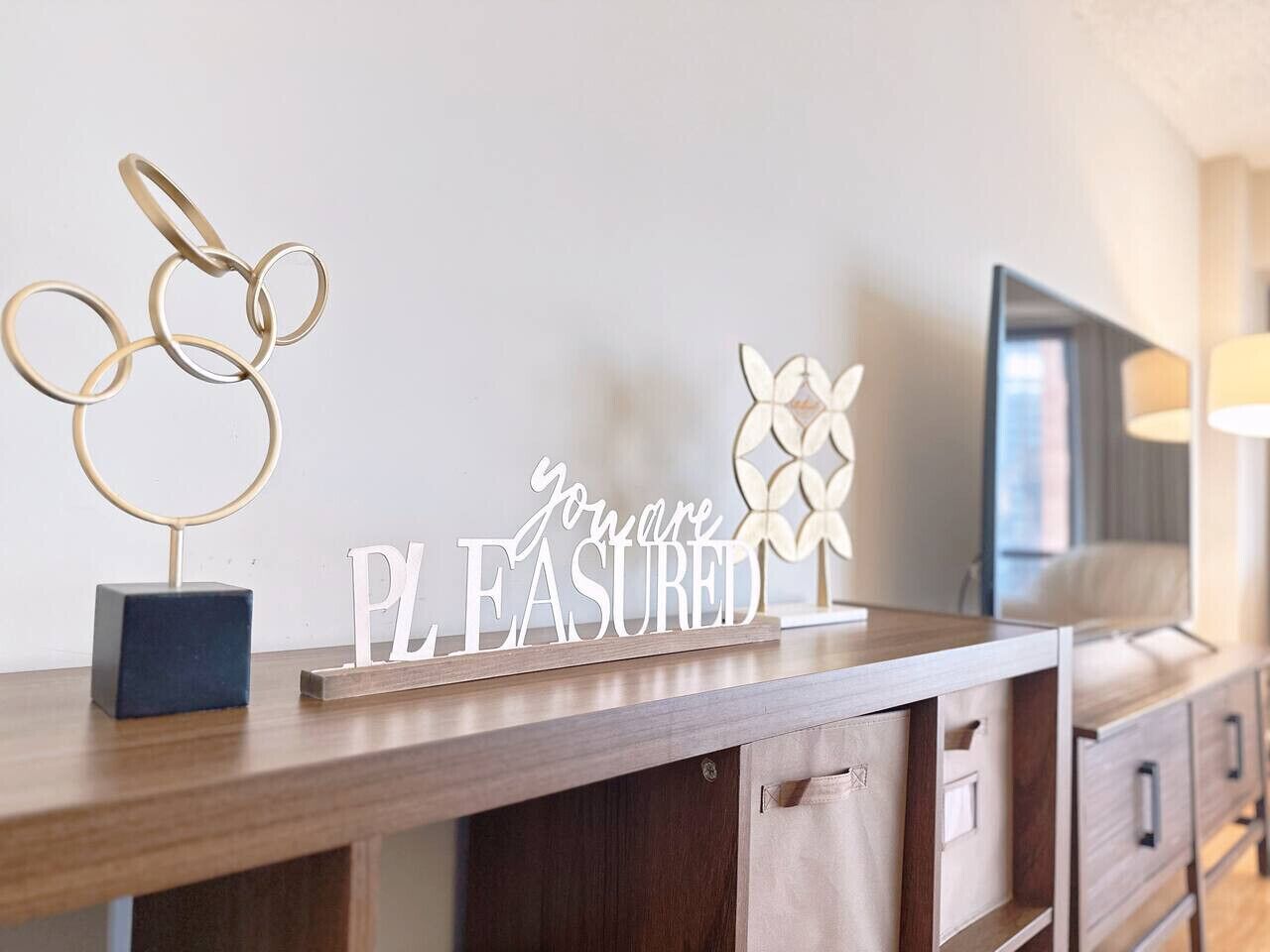A wooden desk with a sign that reads 'you are pleased,' a decorative ring, and a small blue cube.