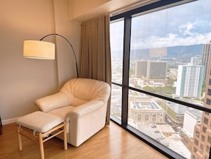 Une chambre moderne dotée d’une grande fenêtre, d’un fauteuil confortable, d’un lampadaire et offrant une vue sur le paysage urbain.