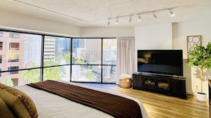Une chambre d’hôtel moderne avec un grand lit, un téléviseur à écran plat, une grande fenêtre donnant sur la ville et une petite plante.