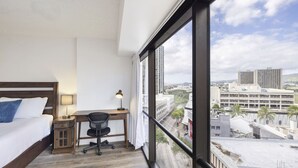Une chambre à coucher comprenant un lit, un bureau, une chaise et une grande fenêtre donnant sur la ville.