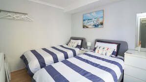 A bedroom with two beds, a painting of a beach scene, a white radiator, and a white dresser. - The Hideaway (Dartmouth)
