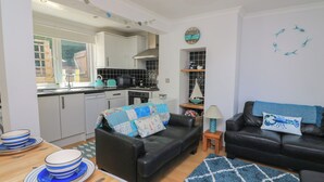 A compact living space with a kitchenette, two black leather sofas, a dining table with blue and white plates, and a blue patterned rug. - The Hideaway (Dartmouth)