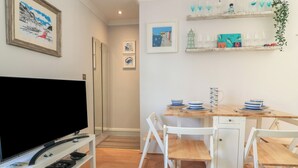 A modern living room with a flat-screen TV, white furniture, and a dining area with a wooden table and chairs. - The Hideaway (Dartmouth)