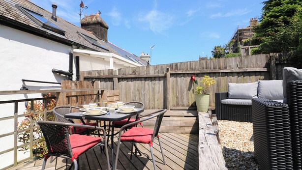 A wooden deck with outdoor furniture, including a table and chairs, and a wicker sofa. - The Hideaway (Dartmouth)