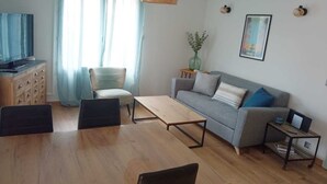 Un salon comprenant un canapé, deux fauteuils, une table basse, un téléviseur et une petite table d’appoint sur laquelle est posé un vase.