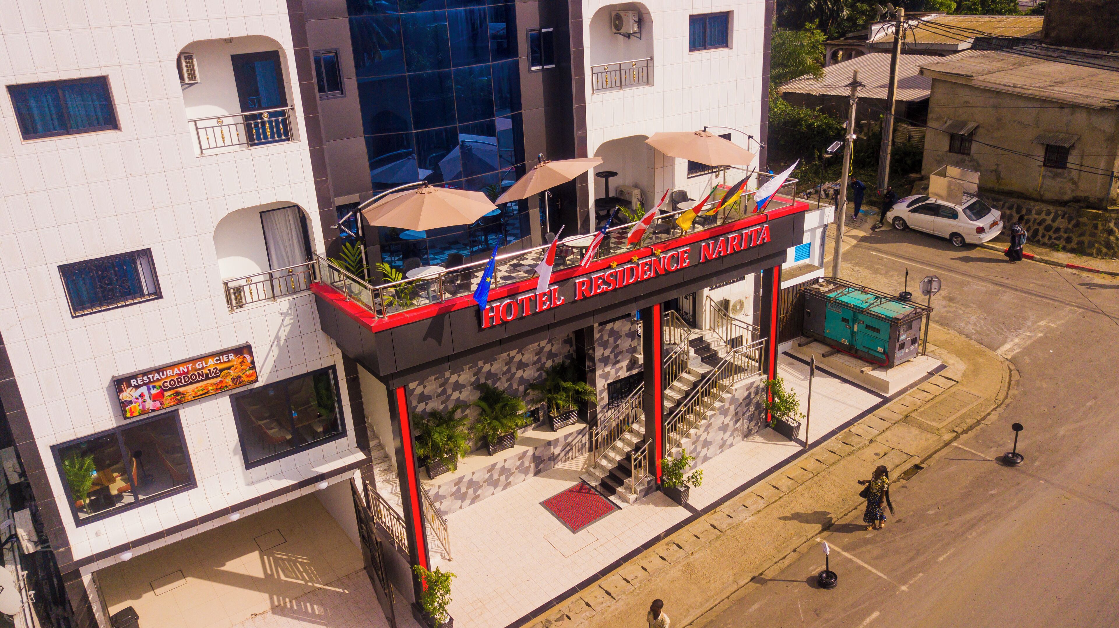 Un hotel con fachada roja y negra, varios balcones con sombrillas, y un cartel que dice 'HOTEL RESIDENCE NARITA'.
