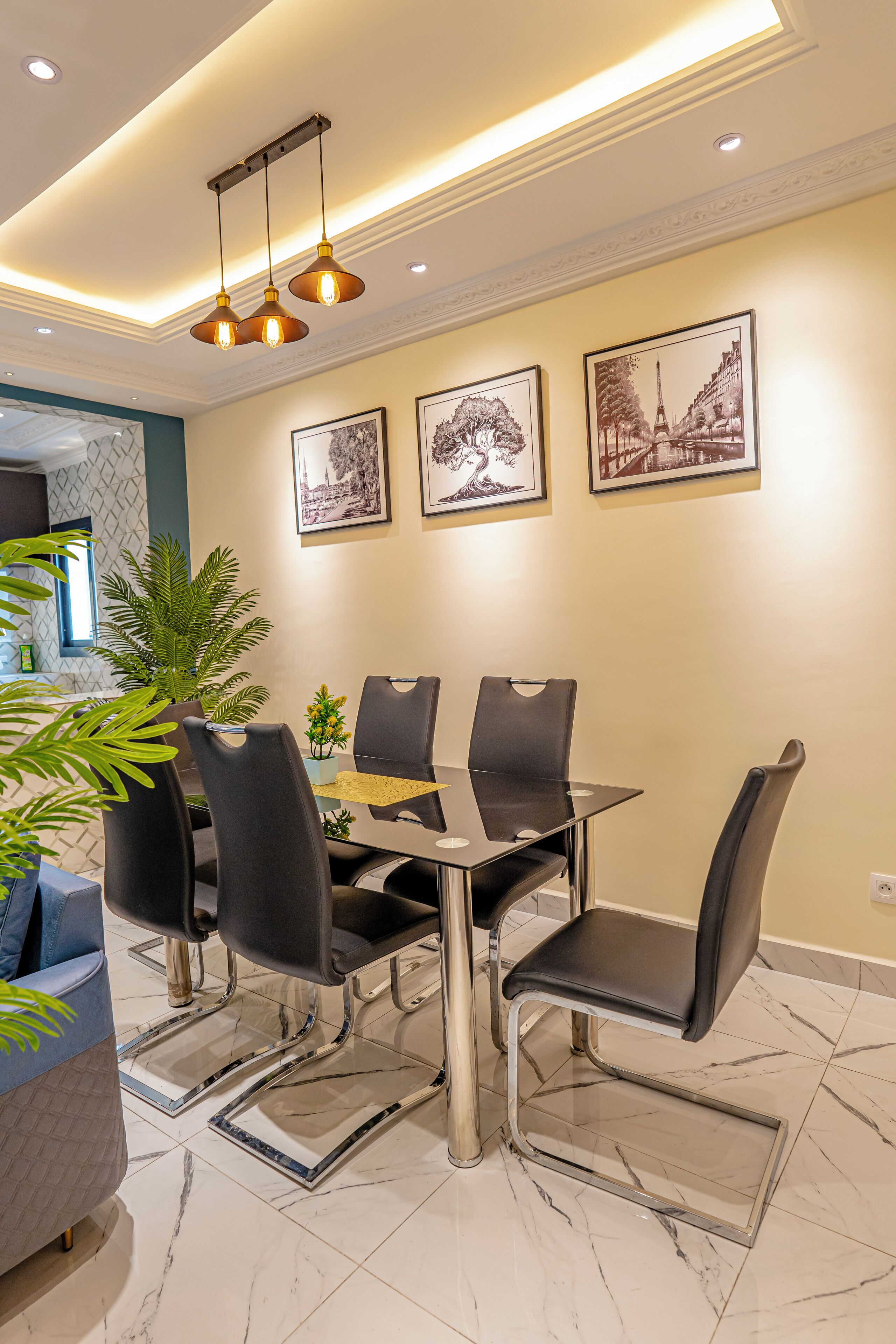 A dining area with a table and chairs, a potted plant, and framed pictures on the wall.