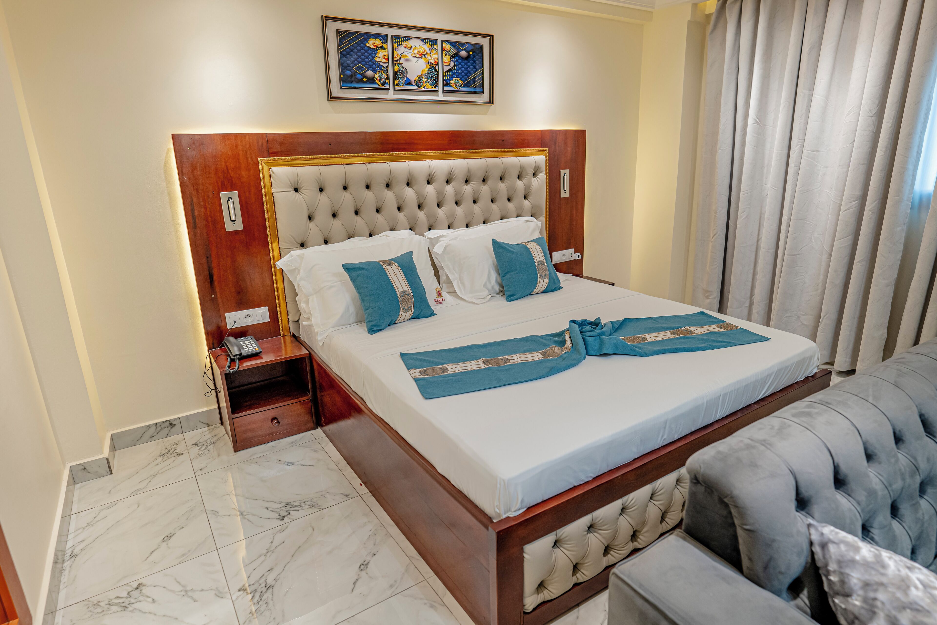 Ein Hotelzimmer mit einem großen Bett, einem hölzernen Kopfteil, einem Nachttisch mit Telefon und einer blau-weißen Bettdecke.