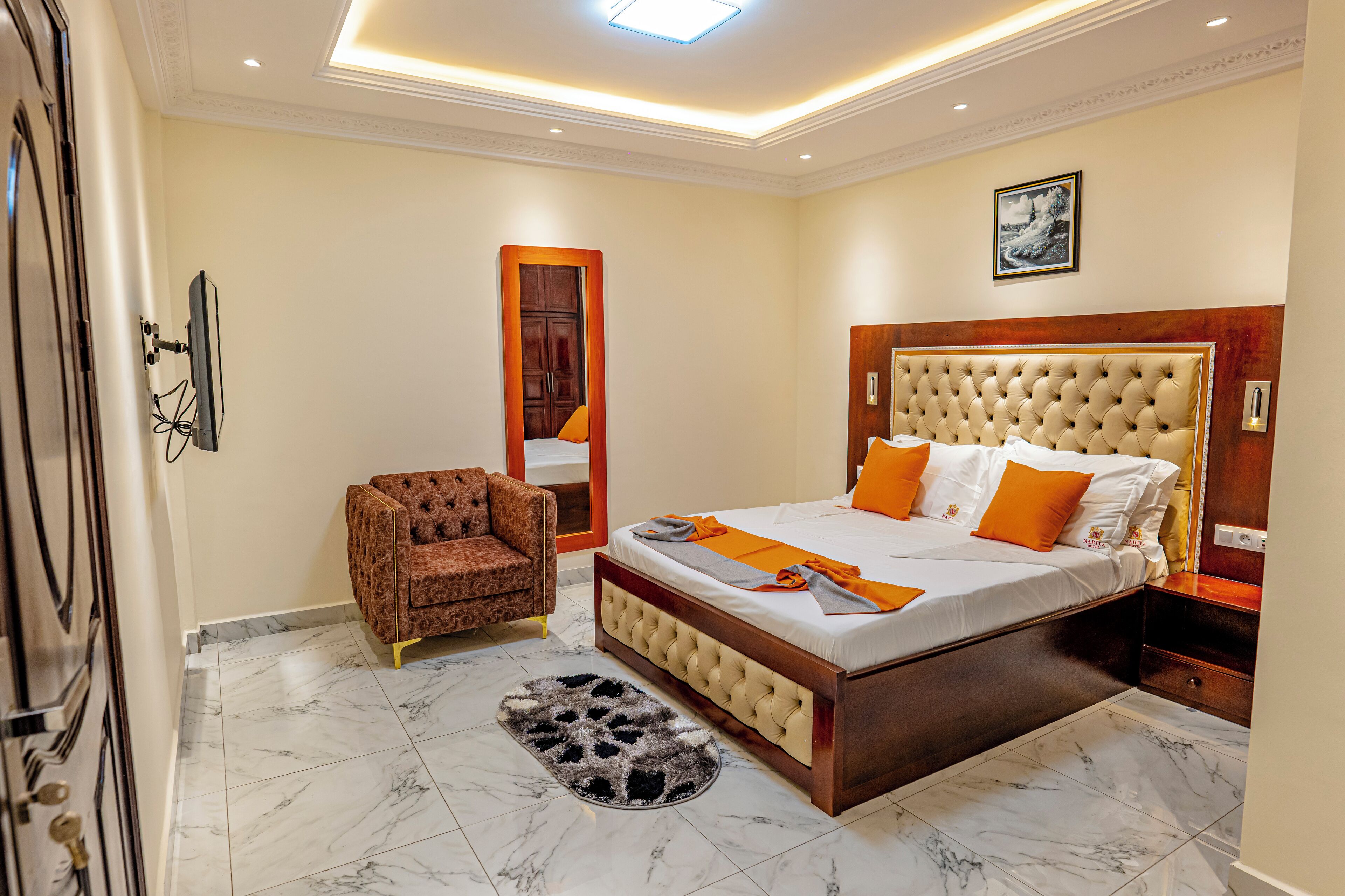 A bedroom with a large bed, a chair, a wooden headboard, a mirror, and a marble floor.