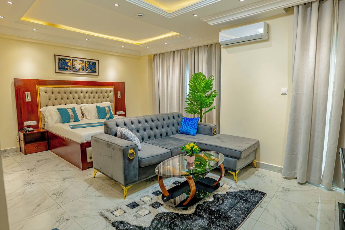 A modern bedroom with a large bed, a grey sofa, and a glass coffee table.