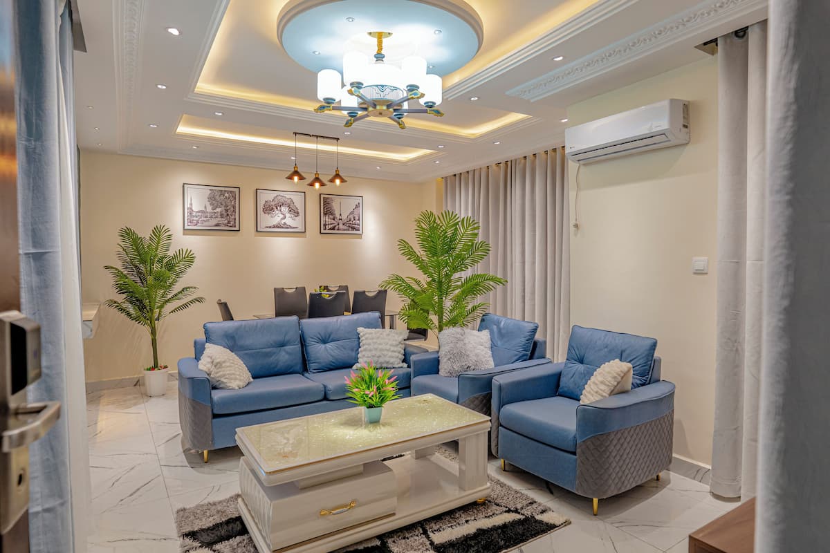 A modern living room with blue sofas, a glass coffee table, and two potted plants.
