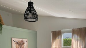 Ett modernt vardagsrum med en beige soffa, ett soffbord och ett matbord med stolar. Det finns en svart hänglampa, en bordslampa och en inramad tavla på väggen.