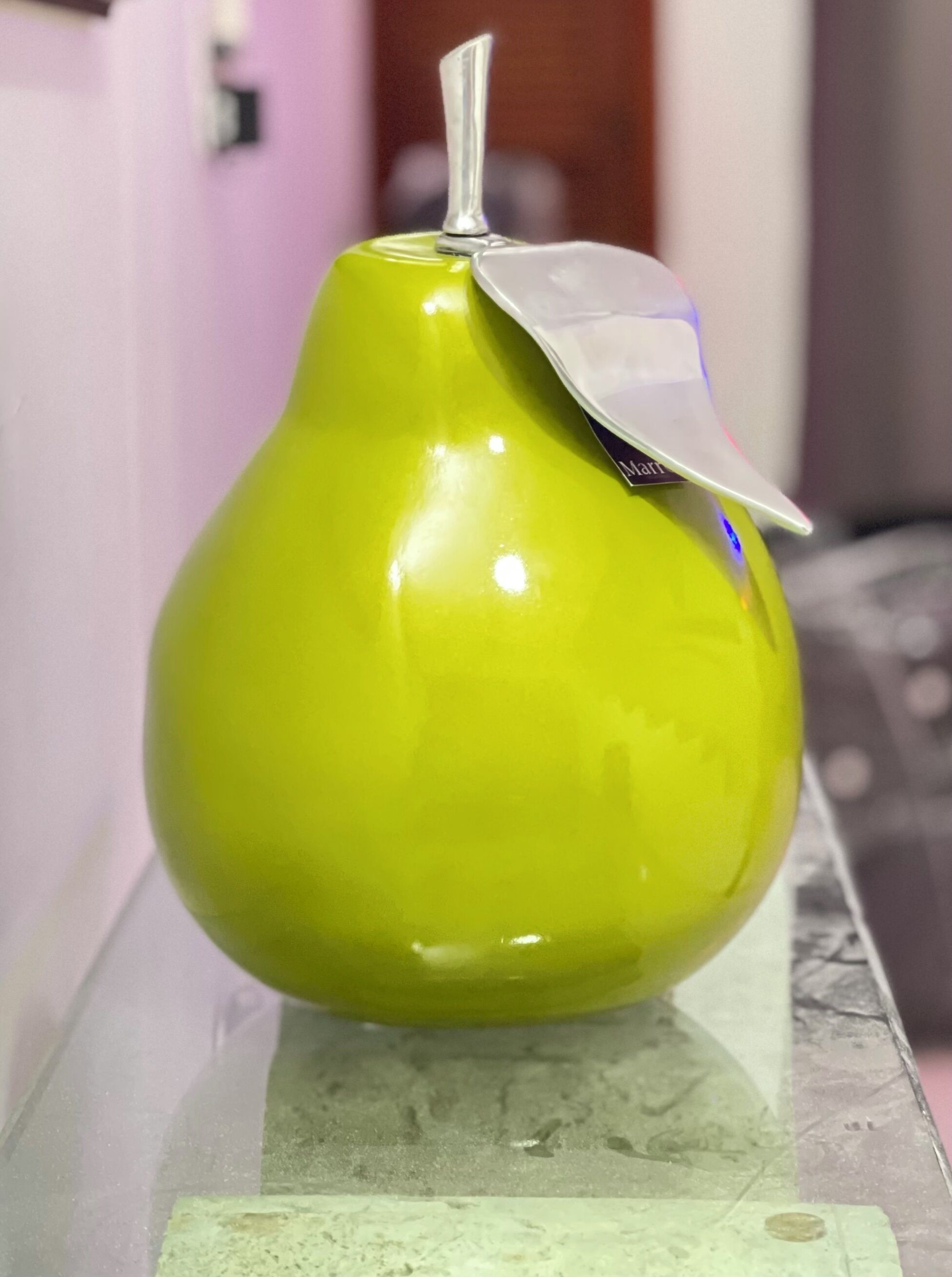 Un objet vert en forme de poire, posé sur une surface réfléchissante.