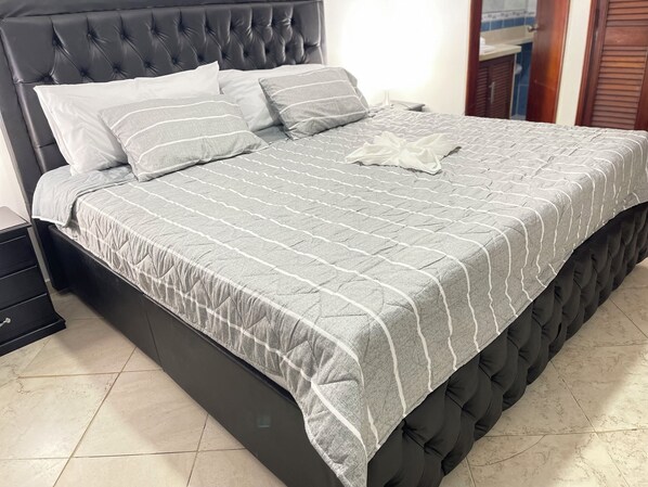 A bed with a grey quilt and white pillows, a dark headboard, and a wooden nightstand to the left. - Amazing 2bedroom duplex near the beach (Bolívar)