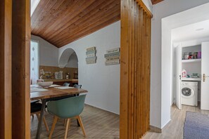 Zona de menjador amb taula i cadires de fusta, cuina amb rentadora i decoració de motivació a la paret.