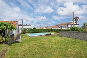 A backyard with a swimming pool, a stone wall, and a white building with a clock tower.