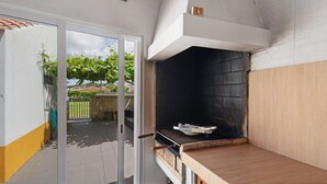 Ein Outdoor-Kochbereich mit Grill, einer Glastür und Blick auf einen Garten.