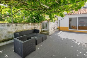 An outdoor seating area with a pergola, a stone wall, and a building with a tiled roof.