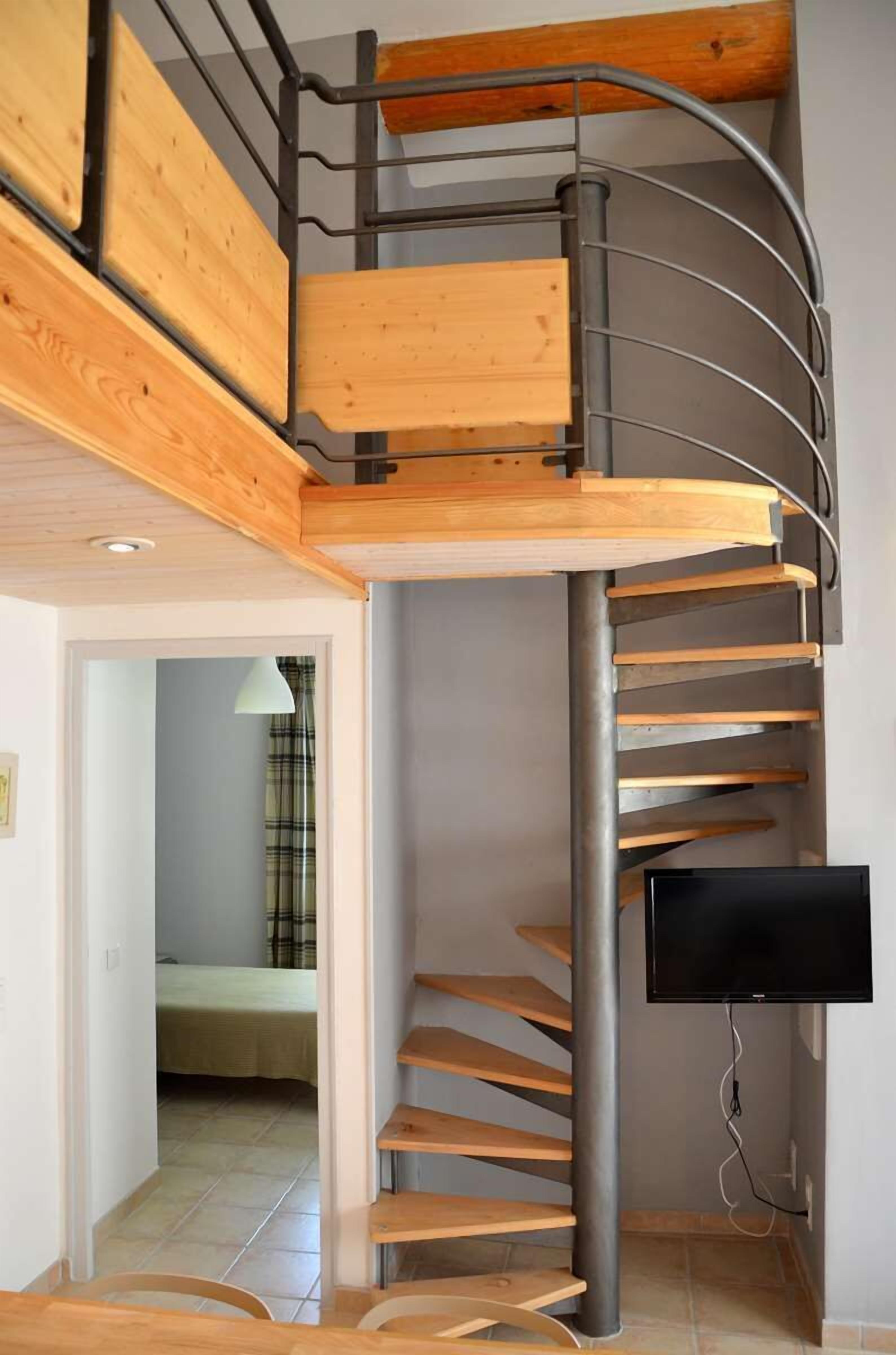 Un escalier en colimaçon avec des marches en bois et des rampes en métal, menant à l’étage supérieur.