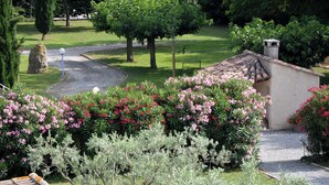 Un jardin avec un chemin de gravier, un petit bâtiment doté d’un toit en tuiles et divers arbustes à fleurs.