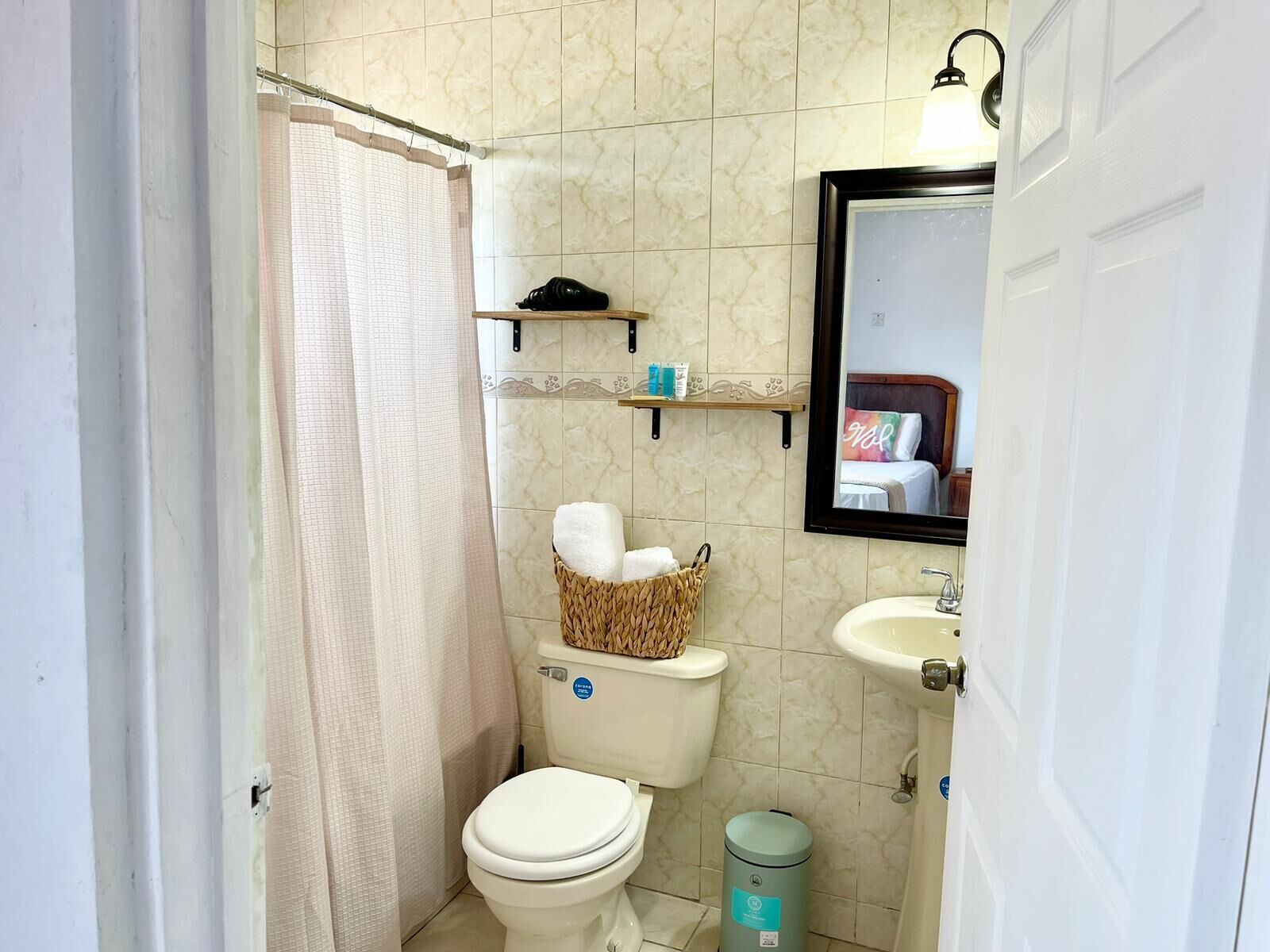 Ein kleines Badezimmer mit Toilette, Waschbecken, Spiegel, Duschvorhang und Mülleimer.