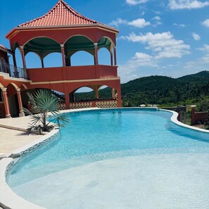 A swimming pool with a gazebo structure, surrounded by a landscaped area and a mountainous backdrop.