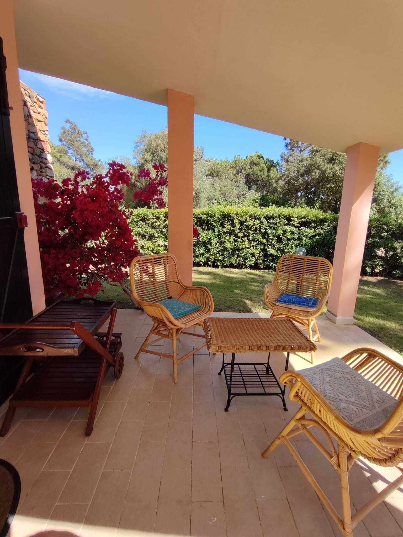 A covered patio area with wicker furniture, including two chairs and a small table, and a wooden cart.