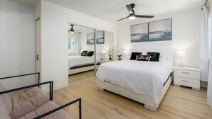 Une chambre à coucher avec un lit, des tables de chevet, un ventilateur de plafond et un grand miroir.