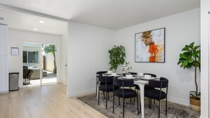 Un espace repas moderne avec une table ronde, des chaises noires, un tapis gris et un grand tableau abstrait accroché au mur.