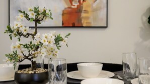 Une table à manger agrémentée d’un bonsaï en guise de centre de table, de verres transparents, d’assiettes blanches et d’une peinture abstraite minimaliste accrochée au mur.