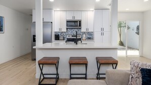 Une cuisine moderne avec des meubles blancs, un îlot central doté de tabourets et une vue sur l’extérieur.