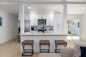 A modern kitchen with white cabinets, a central island with stools, and a view to the outside.