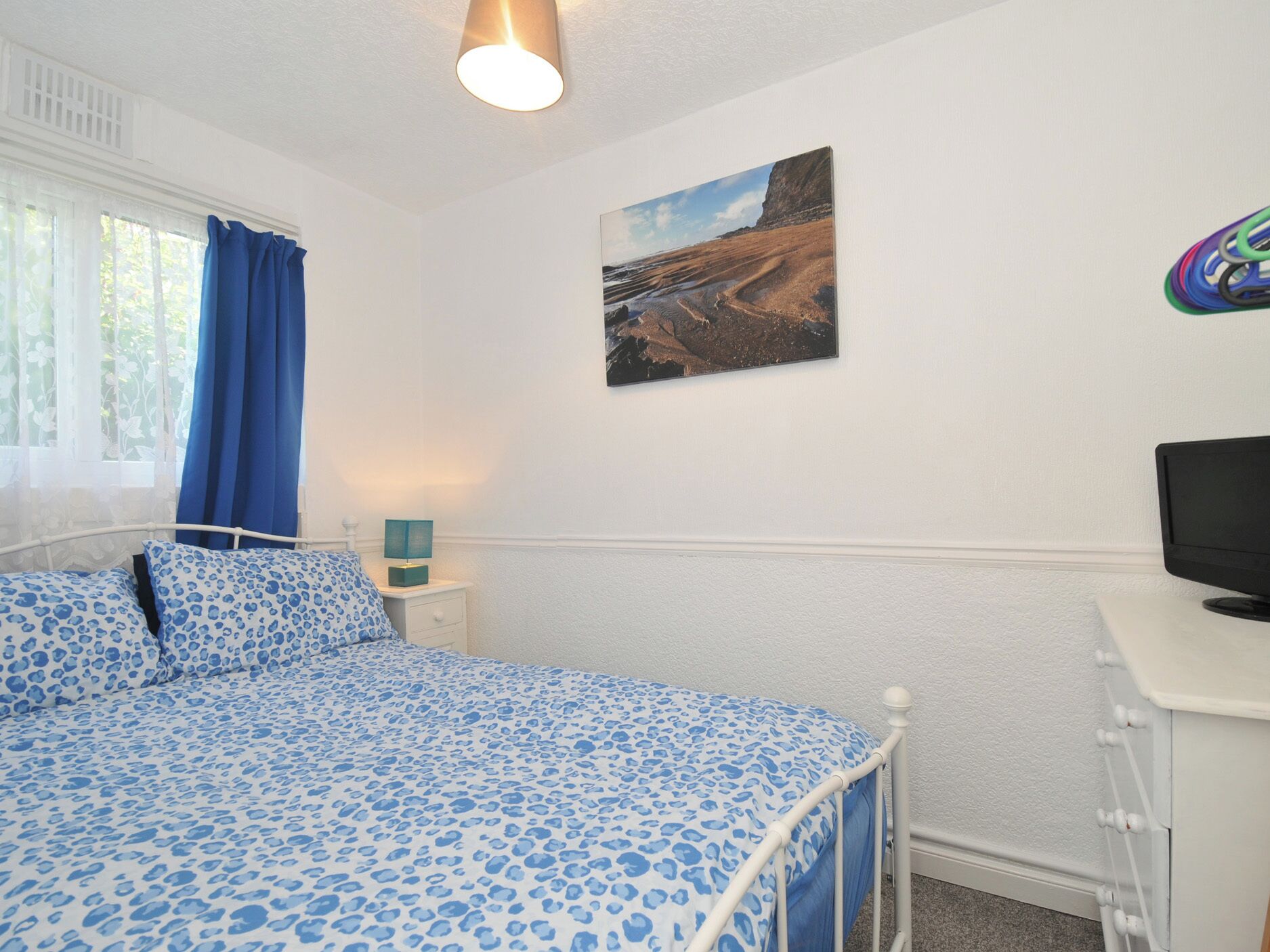 A bedroom with a bed, a bedside table, a lamp, a TV, and a painting on the wall.
