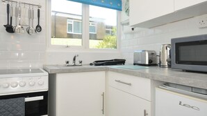 A kitchen with white cabinets, a stove, a microwave, and a toaster. - 8 Hillside (Bude)