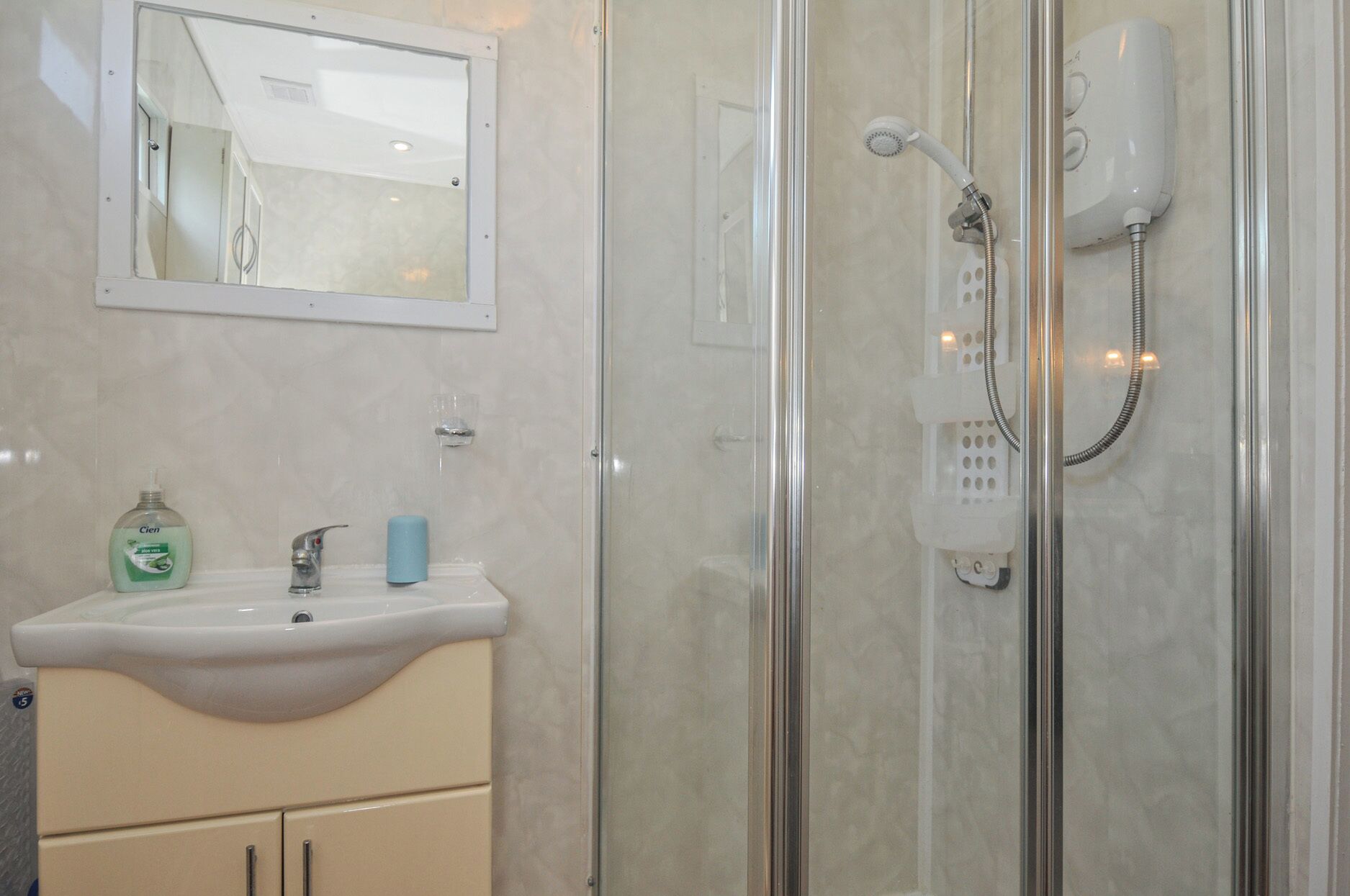 A bathroom with a glass-enclosed shower, a white sink, and a mirror above the sink.