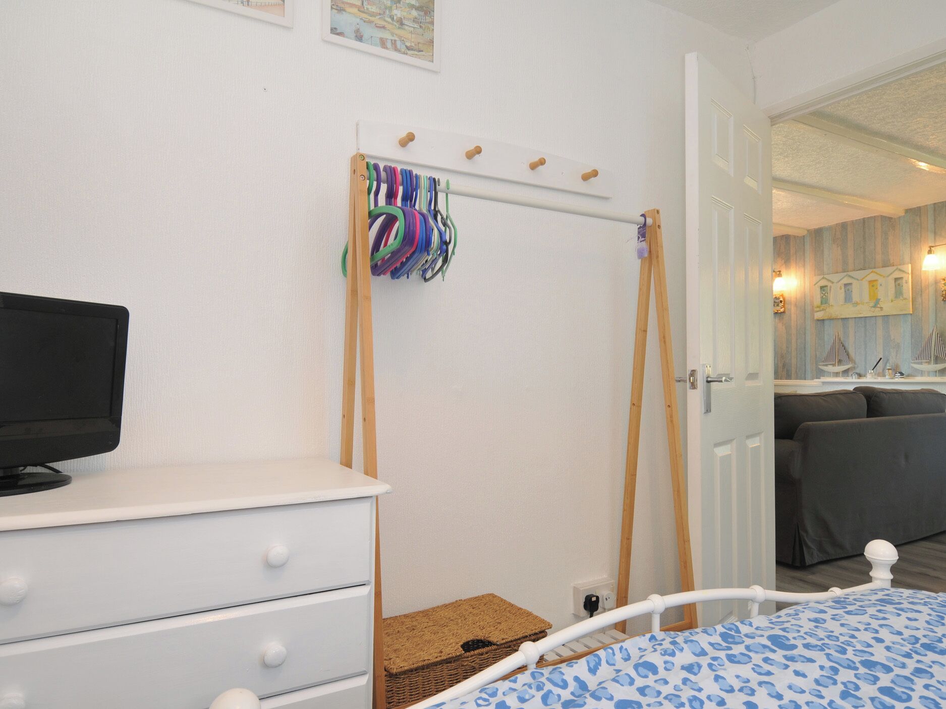 A bedroom with a bed, a TV on a dresser, a wooden rack with colorful items, and a door leading to another room.