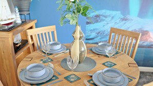 Une table de salle à manger ronde en bois, mise avec des assiettes bleues, des couverts en argent et un vase contenant des feuilles vertes.
