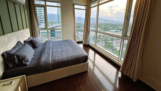 Ein Schlafzimmer mit einem großen Bett, Blick auf eine Stadtlandschaft durch große Fenster und einem Deckenventilator.