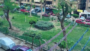 A multi-story residential building with balconies, a parking area with cars, and a small green space with trees. - Your Unique home in cairo (Cairo)