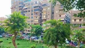 A residential area with multi-story apartment buildings, a parking lot with several cars, and a grassy area with trees. - Your Unique home in cairo (Cairo)
