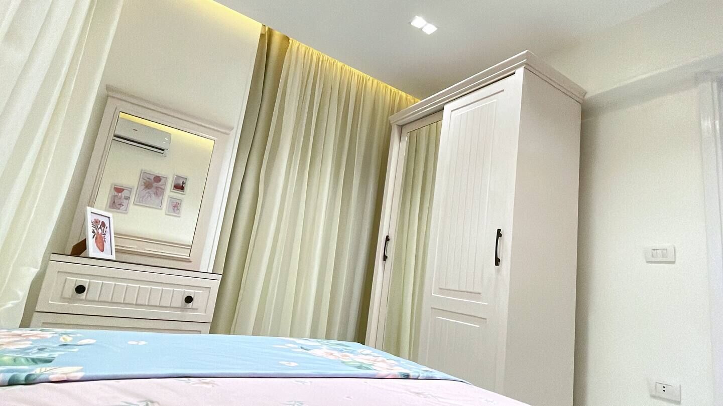 A bedroom with a bed, a dresser, a mirror, a wardrobe, and curtains.