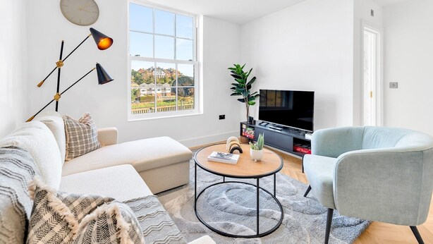 A modern living room with a sofa, armchair, round coffee table, and a TV stand. - Pass the Keys | Bosun's Loft - Superb Views! (Rye)