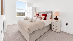 A bedroom with a large bed, a bedside table with a lamp, a window with a view, and a radiator. - Pass the Keys | Bosun's Loft - Superb Views! (Rye)