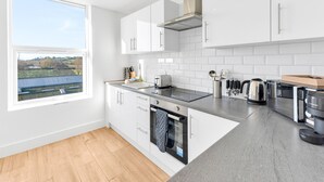A modern kitchen with white cabinets, a built-in oven, a stovetop, and a window overlooking a solar farm. - Pass the Keys | Bosun's Loft - Superb Views! (Rye)