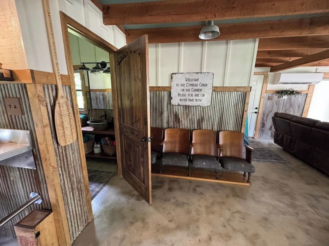 A rustic cabin interior with a wooden bench seating area, a sign welcoming guests to the cabin, and a rustic decor style.