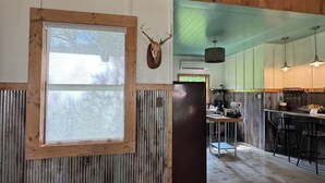 Um interior rústico com teto de madeira, uma janela grande, um chifre de veado na parede e um espaço de bar com banquetas.